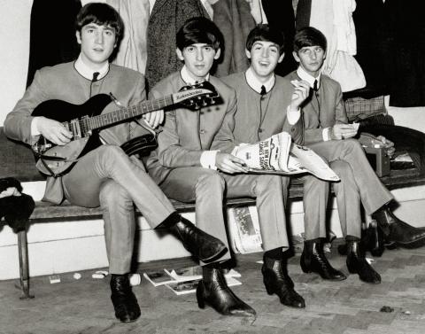 Paul McCartney, John Lennon, George Harrison, and Ringo Starr seated on a bench smiling at the camera.